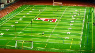 A soccer game at night on a green field with a red logo in the center.