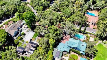 Aerial view of houses with swimming pools and lush trees.