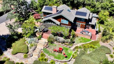 Large house with solar panels surrounded by greenery.