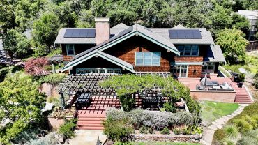 Charming wooden house with solar panels and lush greenery.