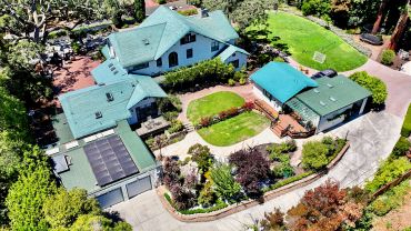 Aerial view of a large house with blue roofs and a green lawn.