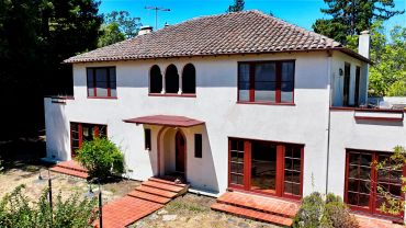 Two-story house with red-trimmed windows and tiled roof.