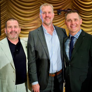 Three men in suits smiling together for a photo.