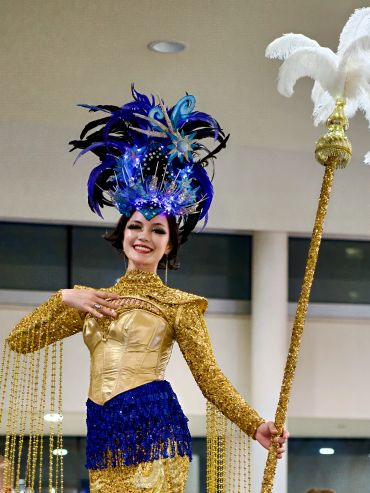 Woman in a glamorous costume with a feathered headpiece and staff.