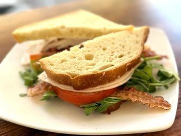 A fresh sandwich with turkey, bacon, tomato, and greens on white bread.