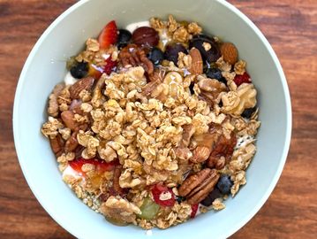 Bowl of granola with mixed nuts, berries, and honey on a wooden table.