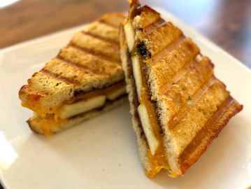 Grilled sandwich with melted cheese and banana slices on a white plate.