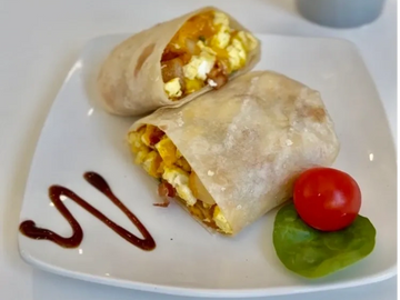 Breakfast burrito halves with scrambled eggs, bacon, and a cherry tomato garnish.