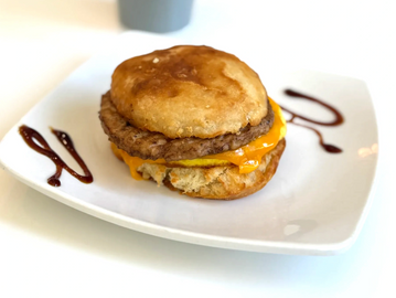 A sausage, egg, and cheese biscuit sandwich on a white plate with decorative sauce.