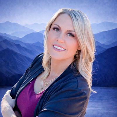 Smiling blonde woman posing with layered mountain backdrop.
