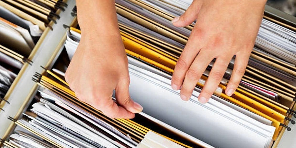 Hands searching through organized hanging file folders filled with documents.