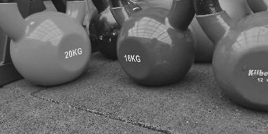 Colorful kettlebells of various weights lined up on a gym floor.