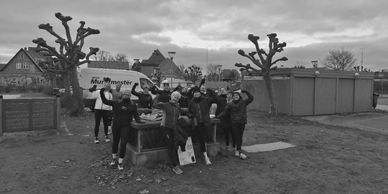 A group of people joyfully posing outdoors near trimmed trees and houses.