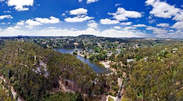 Daylesford, Victoria. Panoramic view of lake under a bright blue sky with scattered clouds.