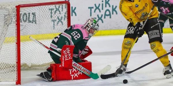 Ice hockey goalie in pink and green gear blocking a shot near the goal.