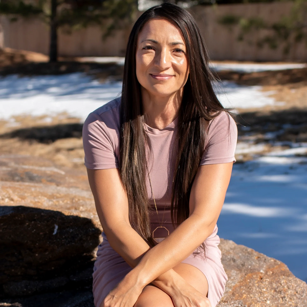 Woman in a mauve dress sitting outdoors on a rock, smiling gently.