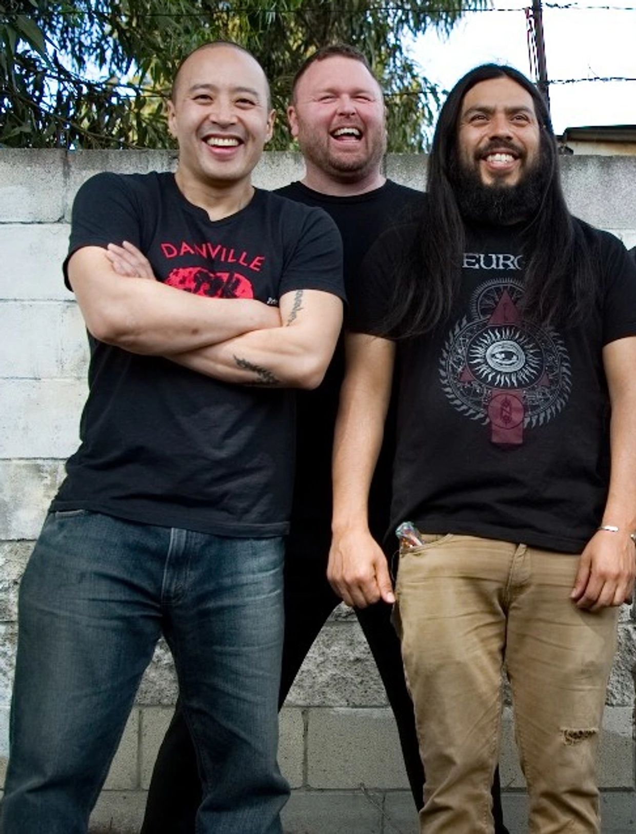 Three men smiling against a wall outdoors.