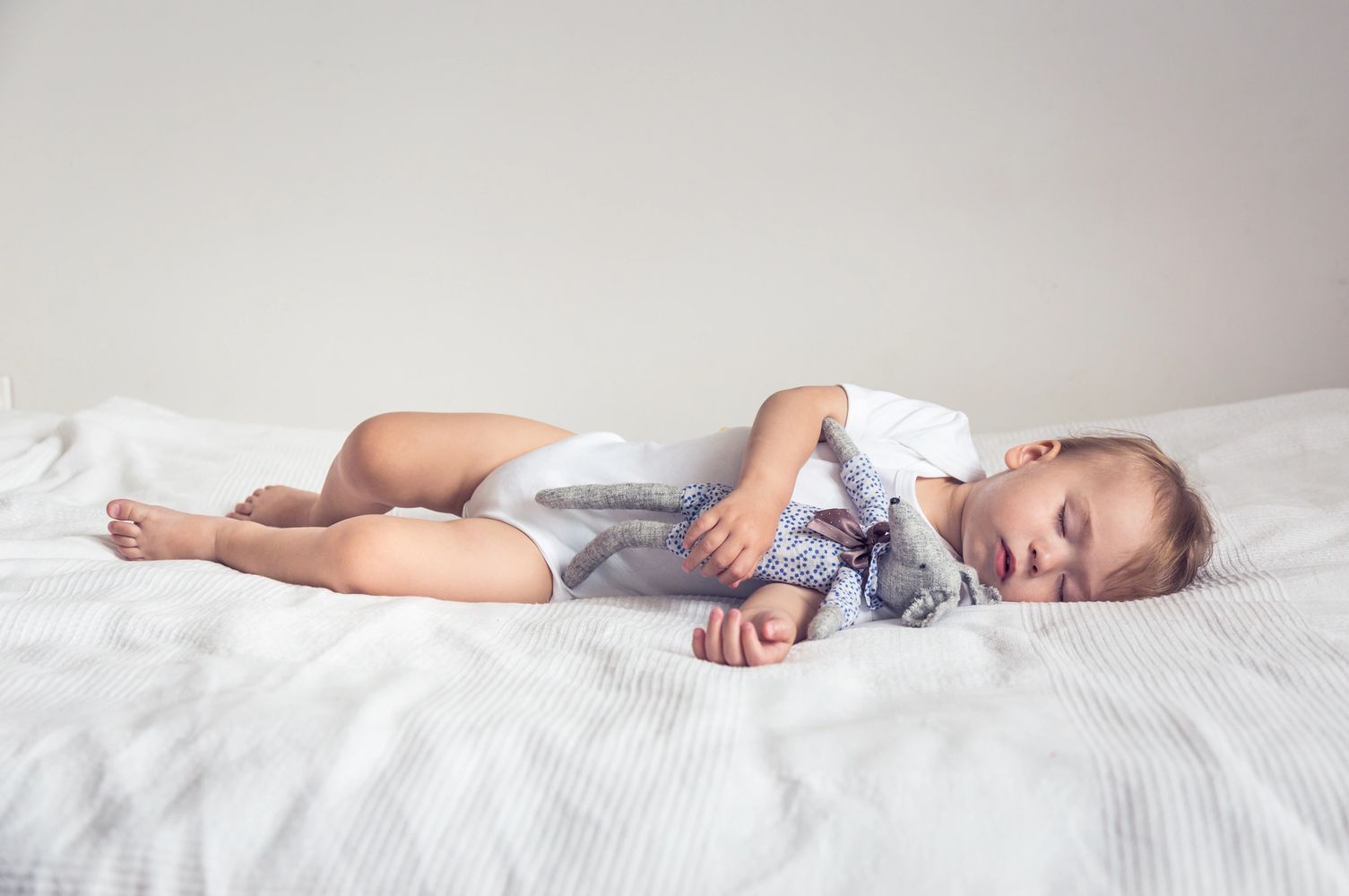 toddler boy lying down on a bed sleeping with a stuffed animal, illinois sleep consultant, toddler