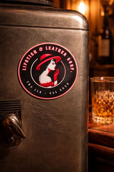 Vintage fridge door with Lipstick & Leather Corp. logo and a glass of whiskey in the background.