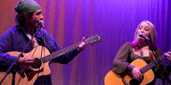 Two musicians playing guitars and singing on stage.