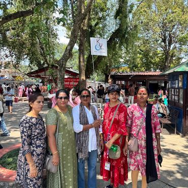 Five women standing outdoors under trees during a sunny day.