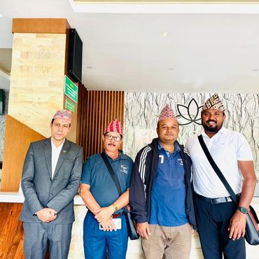 Four men wearing traditional Nepali hats standing indoors, posing for a photo.