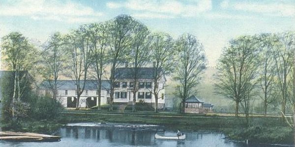 A peaceful house by a lake surrounded by trees on a calm day.