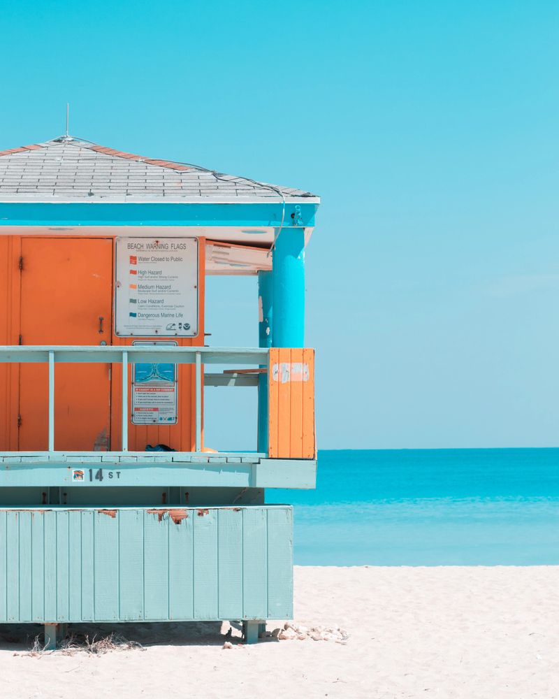 Vibrant blue sea on a white sand beach. Orange and blue painted life guard station. California beach