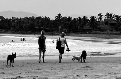 Daytime beach walk at Playa La Saladita—two women and their dogs walking on the sandy beach in a black and white photo.