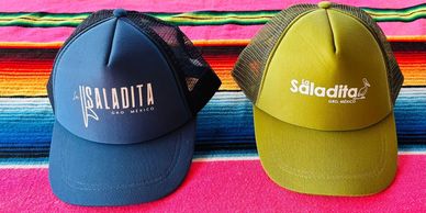 Trucker hat with surfing pelican logo in blue and green—Souvenirs section color photo.