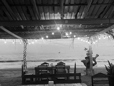 Evening ocean view from Paco’s Restaurant—black and white photo with table, chairs, and palms.