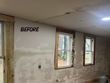 Interior wall renovation in progress with windows and construction materials scattered.