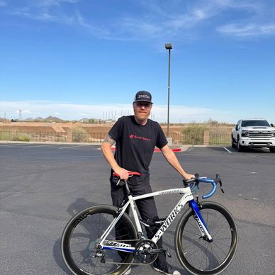 Man standing with a Specialized S-Works road bike in a parking lot under clear skies.