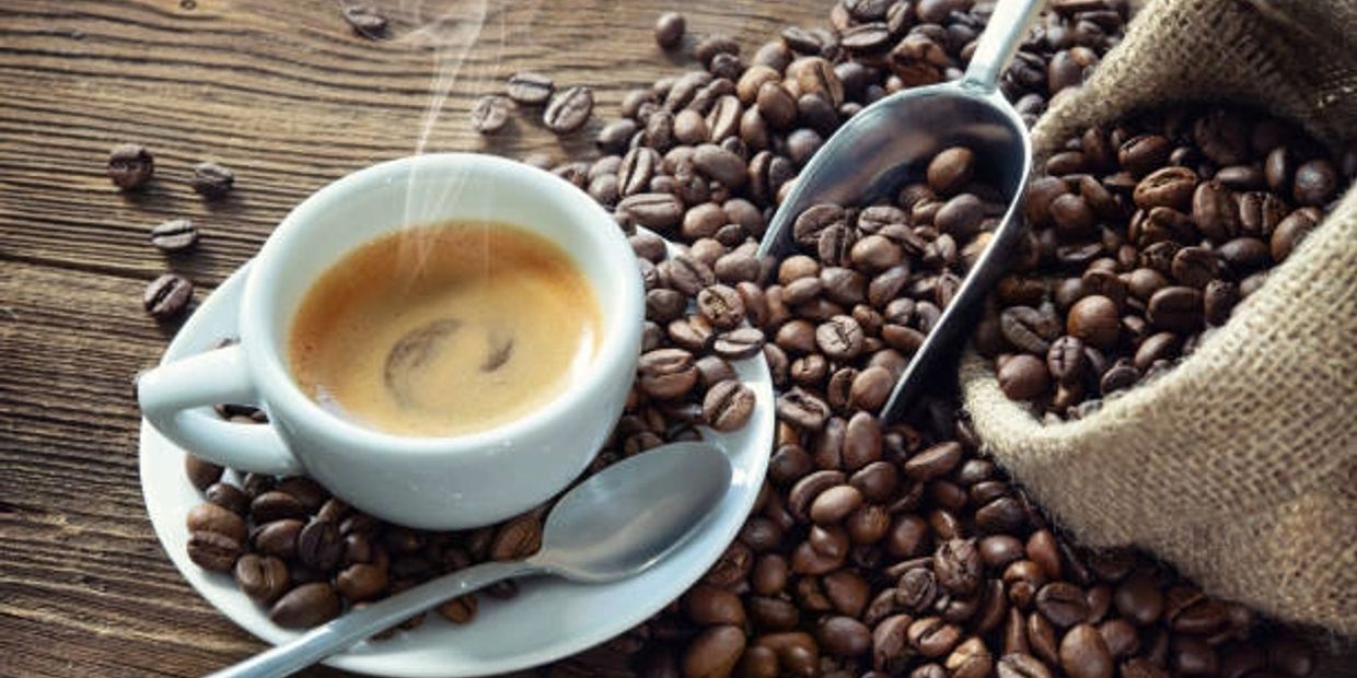 Steaming cup of coffee surrounded by coffee beans and a scoop.