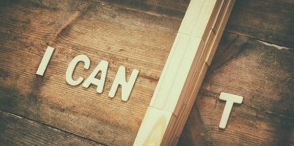 Wooden letters on a rustic surface spell out 'I CAN'T' with a wooden block covering the apostrophe.