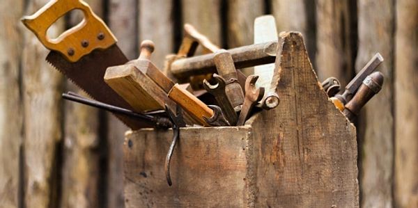 A rustic wooden toolbox filled with various hand tools including a saw and wrenches.