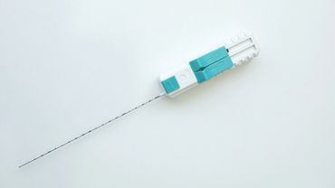 A thin medical biopsy needle with a white and turquoise handle on a white background.