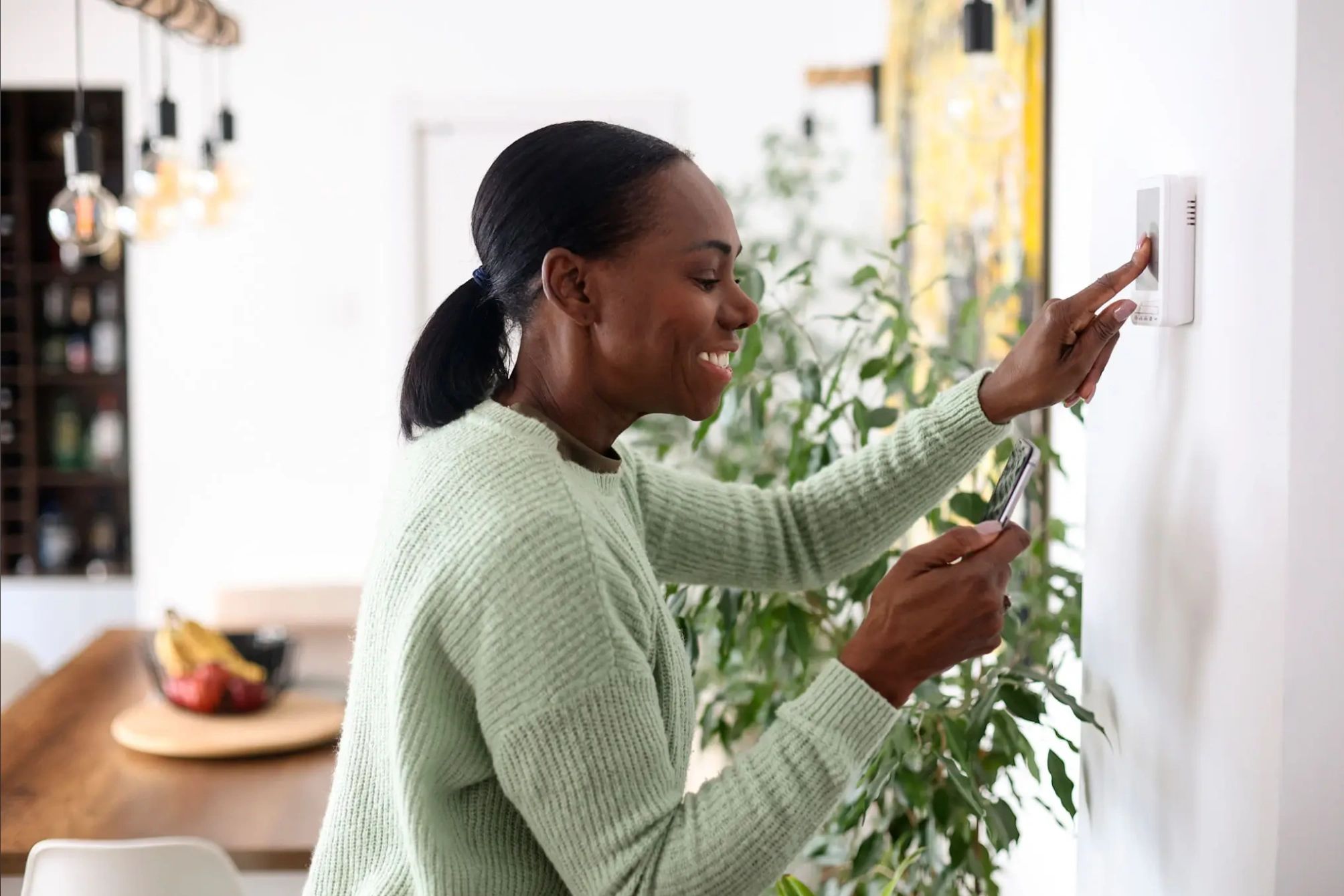 Woman adjusting wall thermostat to set comfortable home temperature for heating or cooling.