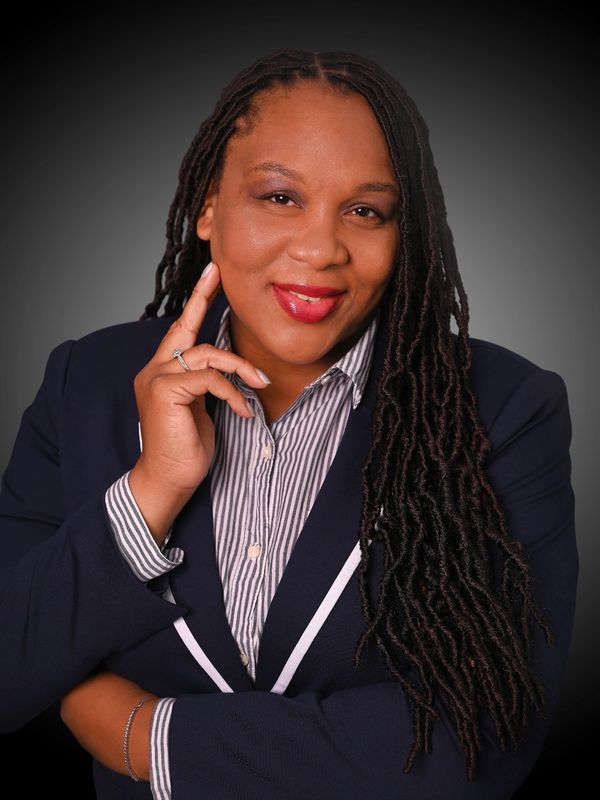 Confident woman with long dreadlocks smiling warmly in professional attire.