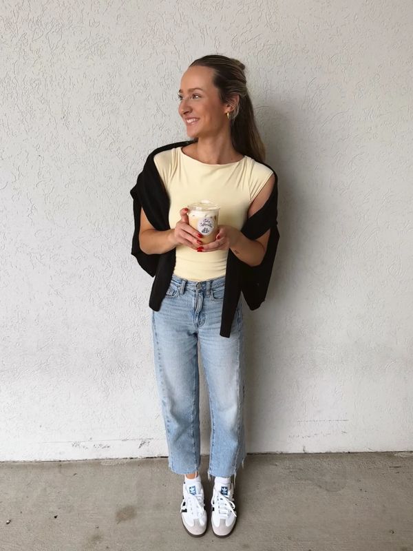 Woman smiling and holding a drink against a textured white wall.