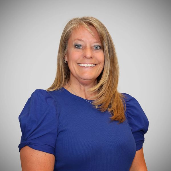 Smiling woman in a blue shirt against a plain backdrop.