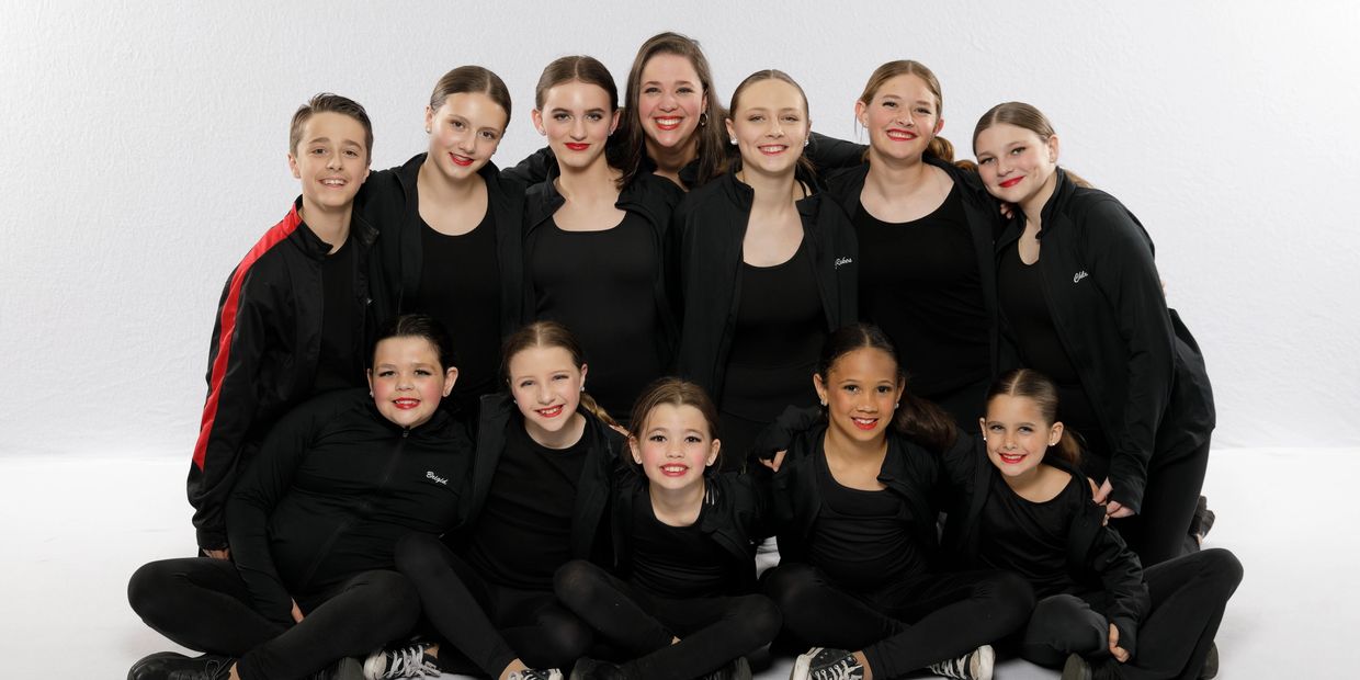 A joyful group of young dancers in black outfits posing together.
