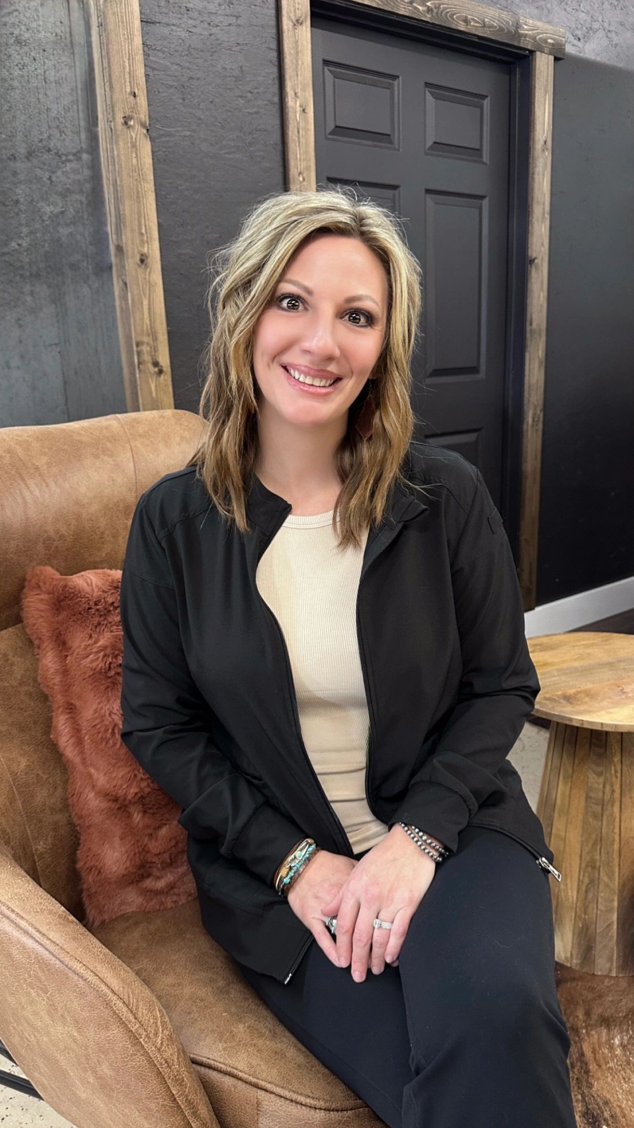 Smiling woman with blonde hair sitting on a brown chair indoors. Peak aesthetics. registered nurse.