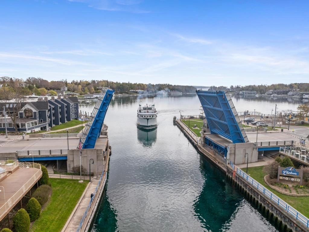 A boat passing through an open drawbridge on a calm river with houses nearby.
