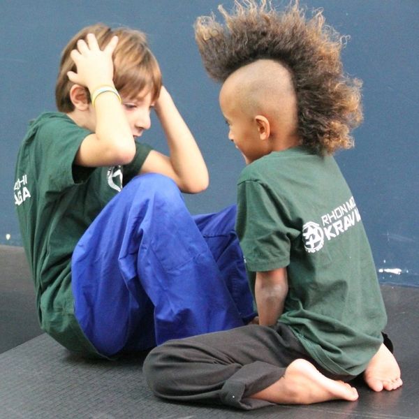 Two children practicing martial arts in green shirts and comfortable pants.