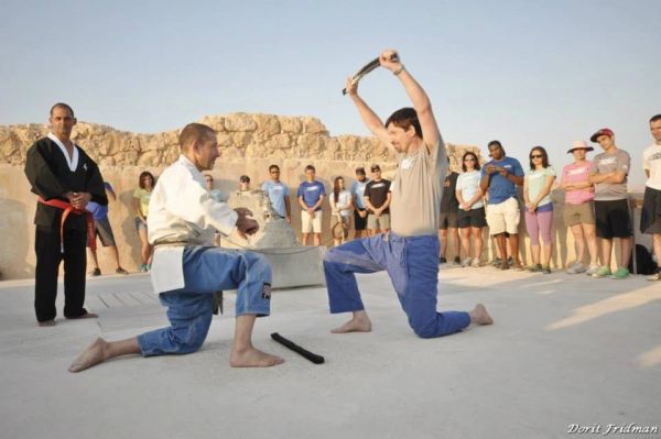Two men practicing martial arts with weapons while a group watches.