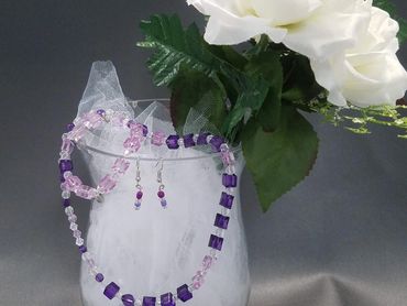 A handmade jewelry set resting on a glass vase accented with white flowers.