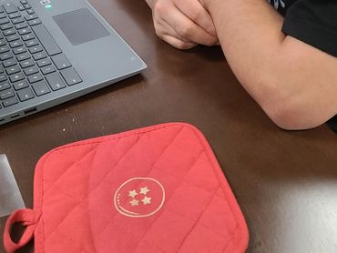 A custom-printed potholder on a desk with a person and a laptop computer.