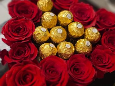 An arrangement of red roses in the shape of a heart filled with golden-wrapped candies.