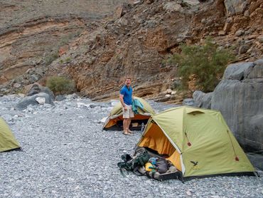 Three green tents set up on rocky terrain with a man standing near one tent.